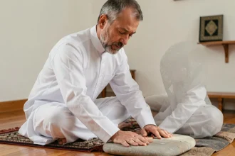 Homme en tenue islamique effectuant le tayammum avec une pierre sur un tapis de prière à domicile
